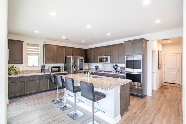 kitchen featuring a kitchen bar, sink, light stone counters, appliances with stainless steel finishes, and an island with sink