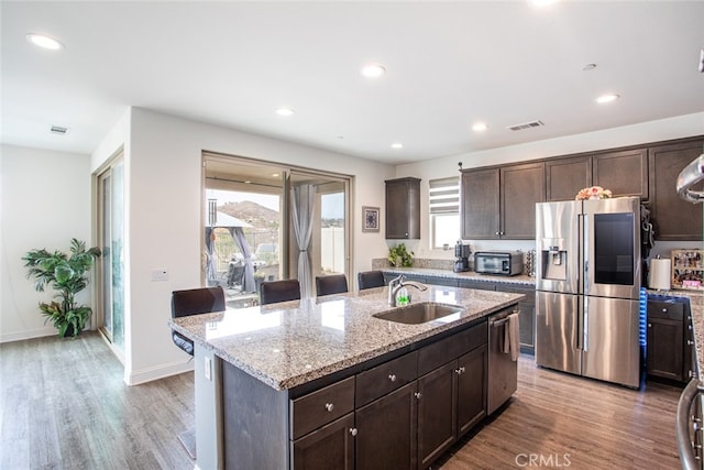 kitchen featuring appliances with stainless steel finishes, sink, a kitchen island with sink, dark brown cabinetry, and light hardwood / wood-style floors