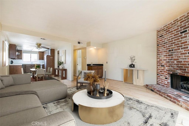 living room with a brick fireplace, light hardwood / wood-style flooring, and ceiling fan