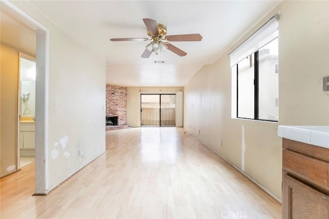 spare room with light hardwood / wood-style flooring, a fireplace, and ceiling fan