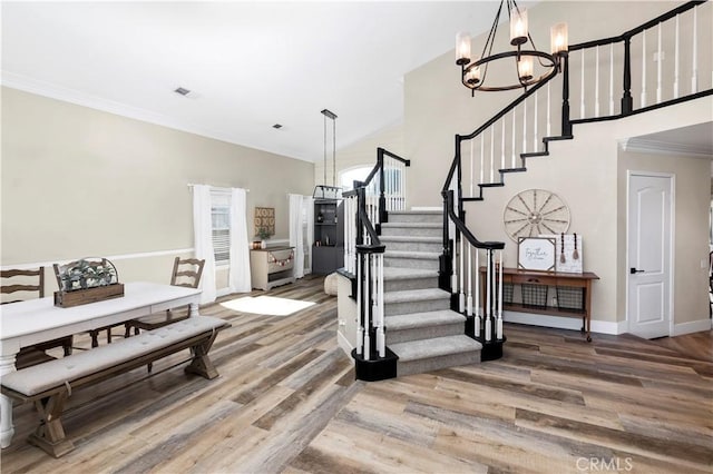 entryway with high vaulted ceiling, an inviting chandelier, hardwood / wood-style flooring, and ornamental molding