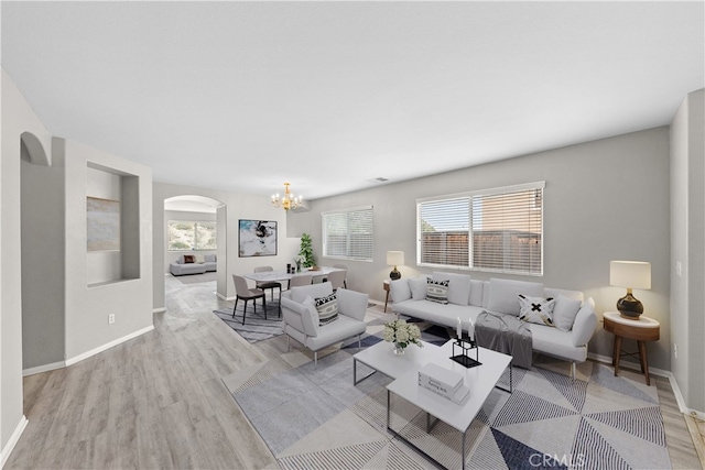 living room with arched walkways, a notable chandelier, visible vents, baseboards, and light wood finished floors