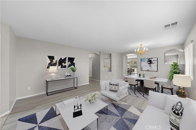 living room featuring baseboards, visible vents, arched walkways, light wood-type flooring, and a notable chandelier