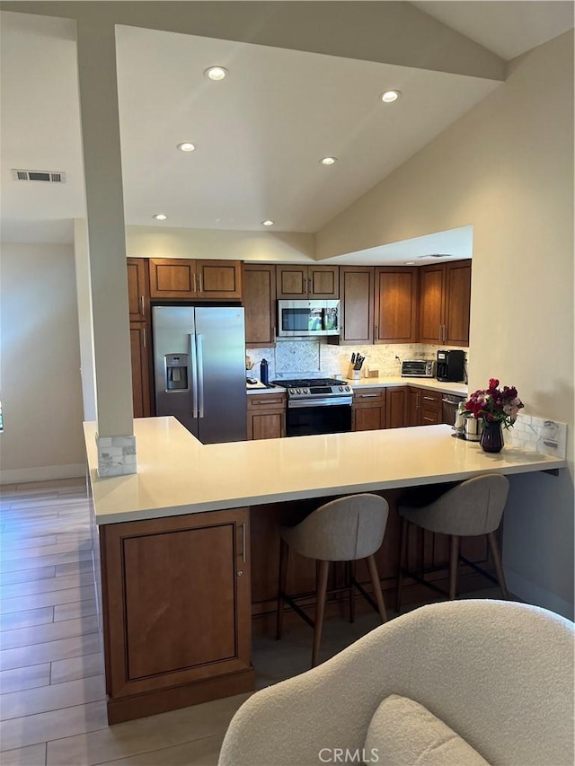 kitchen featuring appliances with stainless steel finishes, lofted ceiling, backsplash, a kitchen bar, and kitchen peninsula