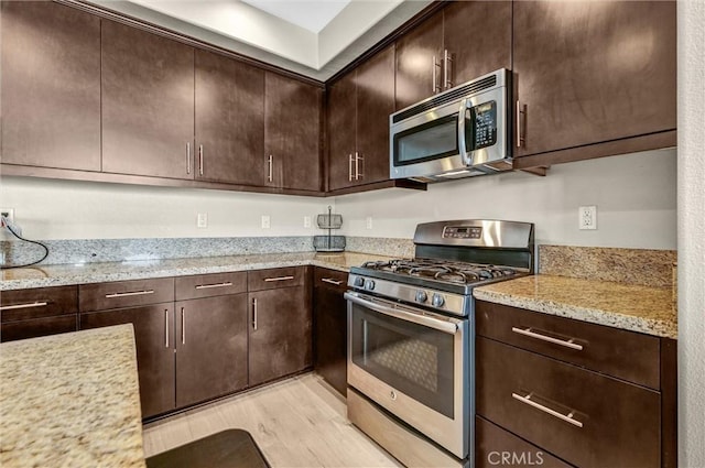 kitchen featuring stainless steel appliances, light wood-type flooring, dark brown cabinets, and light stone countertops