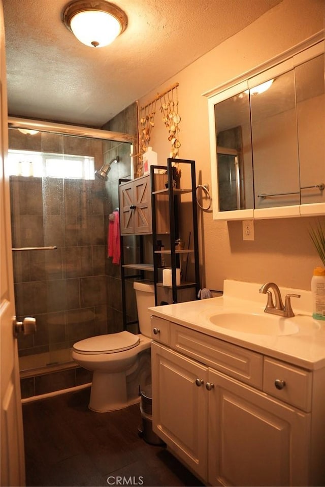 bathroom with vanity, a shower with door, toilet, and a textured ceiling