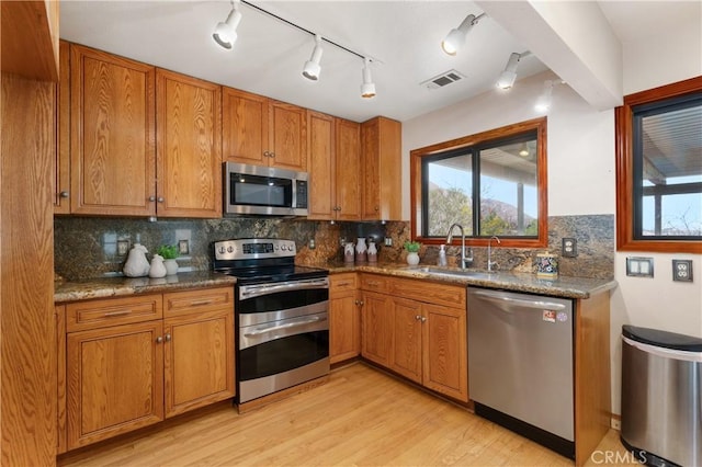 kitchen with sink, light hardwood / wood-style flooring, stainless steel appliances, light stone countertops, and decorative backsplash