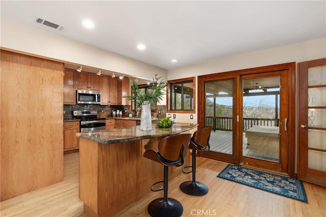 kitchen featuring a kitchen bar, tasteful backsplash, light hardwood / wood-style flooring, dark stone countertops, and appliances with stainless steel finishes