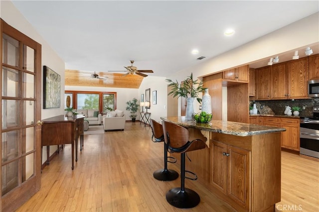 kitchen with decorative backsplash, stainless steel appliances, light hardwood / wood-style flooring, and dark stone counters