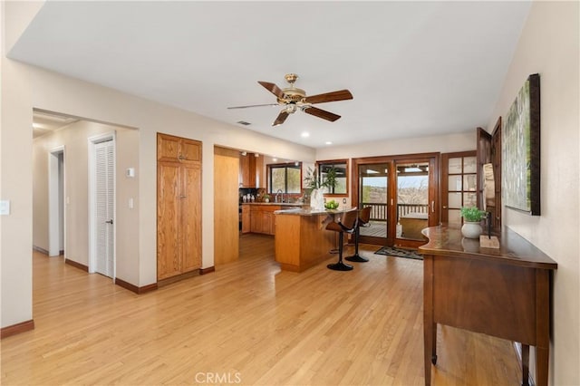 kitchen with sink, light hardwood / wood-style floors, ceiling fan, and a kitchen bar