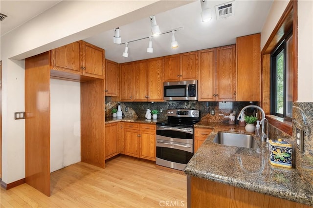 kitchen featuring sink, tasteful backsplash, light hardwood / wood-style flooring, dark stone counters, and stainless steel appliances