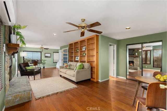 living room featuring ceiling fan, a fireplace, an AC wall unit, and wood-type flooring