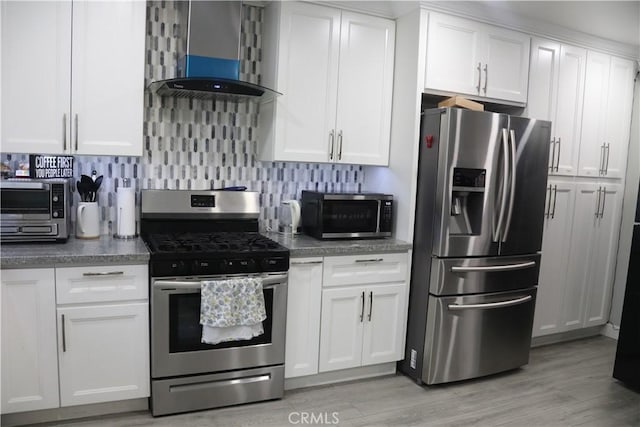 kitchen featuring wall chimney exhaust hood, white cabinetry, light wood-type flooring, appliances with stainless steel finishes, and decorative backsplash