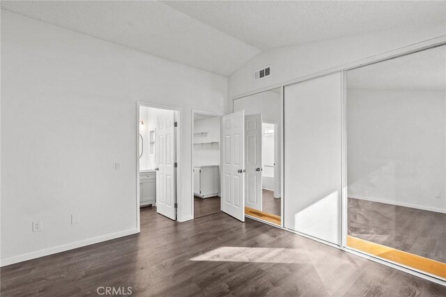 unfurnished bedroom featuring a closet, ensuite bath, vaulted ceiling, and dark hardwood / wood-style floors