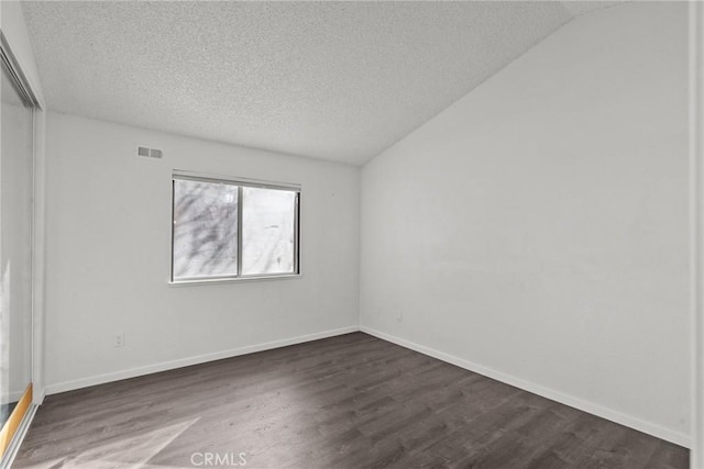 empty room with dark wood-type flooring, vaulted ceiling, and a textured ceiling