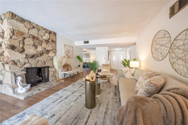 living room featuring hardwood / wood-style flooring, a stone fireplace, and a textured ceiling