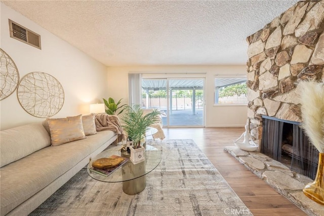 living room with light wood-type flooring, a textured ceiling, and a stone fireplace