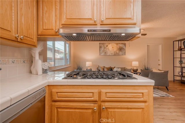 kitchen featuring tile countertops, dishwashing machine, range hood, stainless steel gas stovetop, and light hardwood / wood-style floors