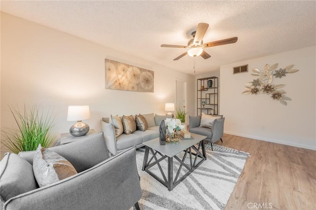 living room with ceiling fan, light wood-type flooring, and a textured ceiling