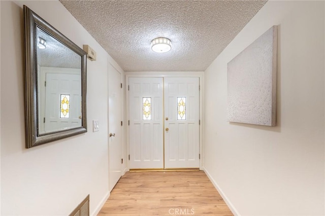 doorway to outside with light wood-type flooring and a textured ceiling