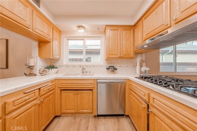 kitchen featuring appliances with stainless steel finishes, sink, backsplash, light hardwood / wood-style floors, and tile counters