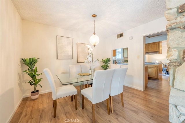 dining room with light wood-type flooring and a textured ceiling