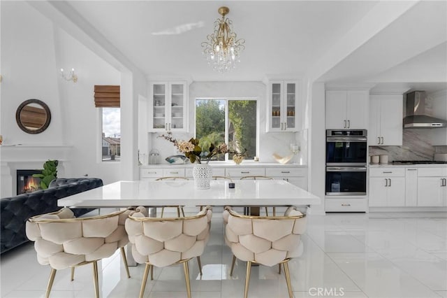 kitchen with pendant lighting, a breakfast bar, appliances with stainless steel finishes, white cabinets, and wall chimney exhaust hood