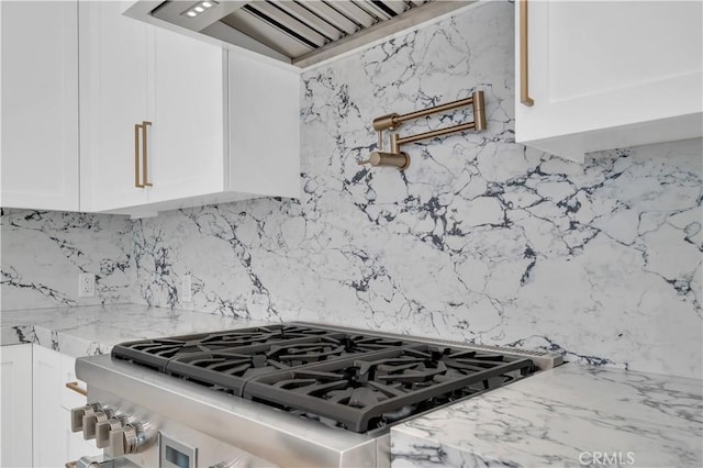 interior details with white cabinetry, light stone countertops, wall chimney range hood, and stainless steel range with gas stovetop