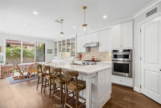 kitchen with sink, crown molding, hanging light fixtures, a kitchen island with sink, and white cabinets