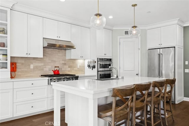 kitchen featuring a breakfast bar area, appliances with stainless steel finishes, white cabinetry, hanging light fixtures, and an island with sink