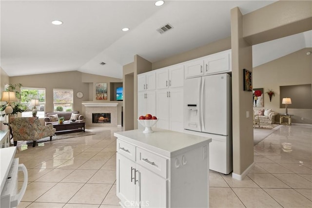 kitchen featuring lofted ceiling, light tile patterned floors, white fridge with ice dispenser, white cabinets, and a kitchen island