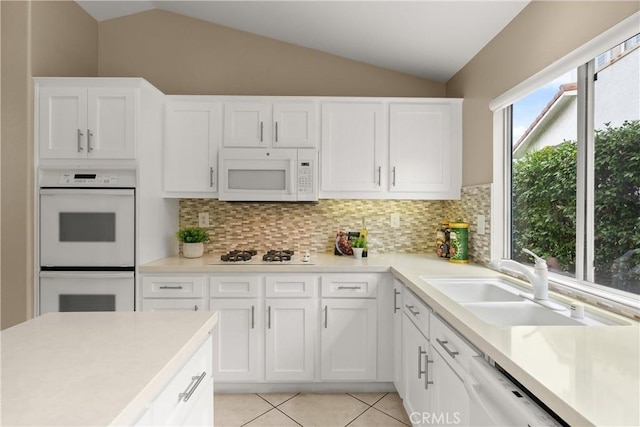 kitchen featuring white cabinetry, lofted ceiling, sink, light tile patterned floors, and white appliances