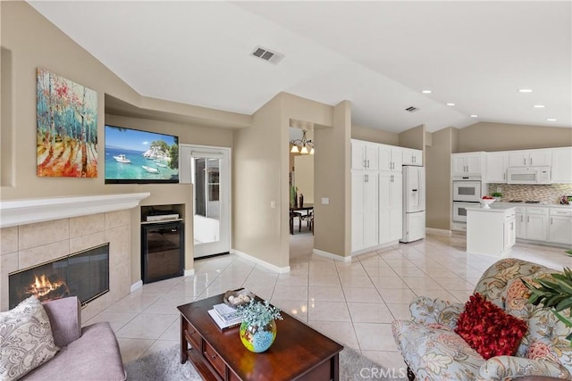 tiled living room with a chandelier, lofted ceiling, and a tiled fireplace