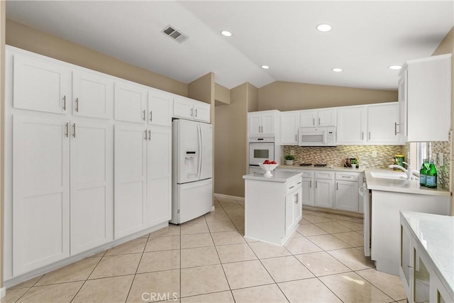 kitchen with lofted ceiling, white cabinetry, a center island, light tile patterned floors, and white appliances