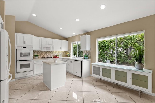 kitchen with backsplash, white appliances, a center island, and white cabinets