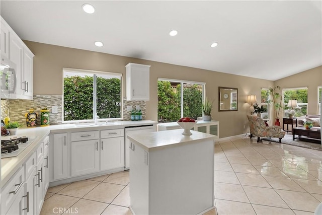 kitchen featuring lofted ceiling, light tile patterned floors, a center island, white cabinets, and decorative backsplash