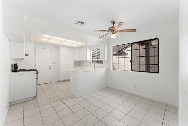 kitchen with visible vents, white cabinets, a sink, and tile counters