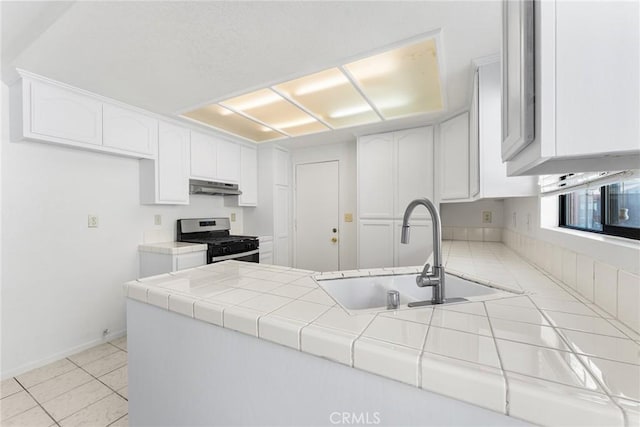 kitchen with under cabinet range hood, a peninsula, stainless steel gas stove, white cabinets, and a sink