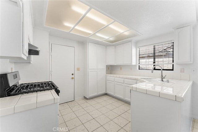 kitchen featuring tile countertops, stainless steel gas stove, white cabinets, and a sink