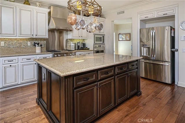 kitchen with stainless steel appliances, hanging light fixtures, decorative backsplash, ornamental molding, and wall chimney range hood