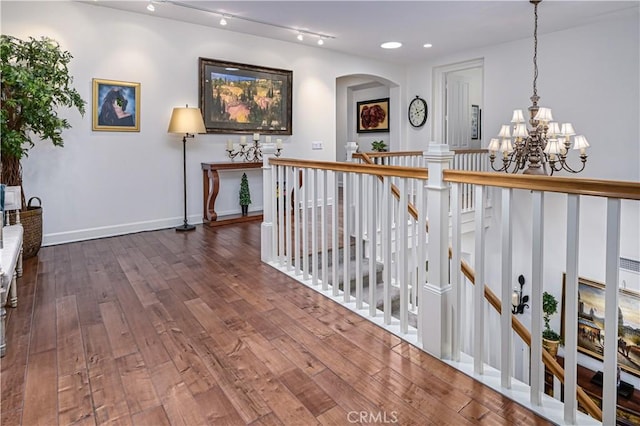 corridor featuring baseboards, arched walkways, dark wood-style flooring, an upstairs landing, and a chandelier