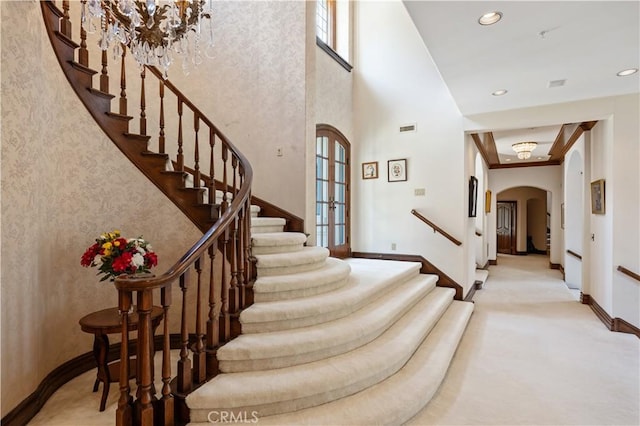 staircase with arched walkways, recessed lighting, visible vents, a towering ceiling, and baseboards