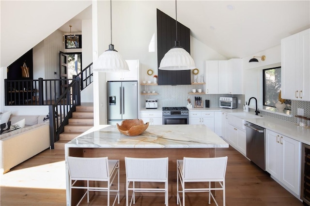kitchen with sink, appliances with stainless steel finishes, white cabinetry, a kitchen island, and decorative light fixtures