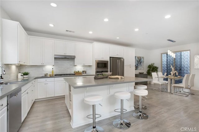 kitchen with a kitchen island, appliances with stainless steel finishes, decorative light fixtures, white cabinetry, and sink