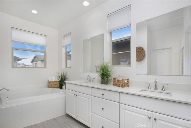 bathroom with vanity, tiled tub, and a healthy amount of sunlight