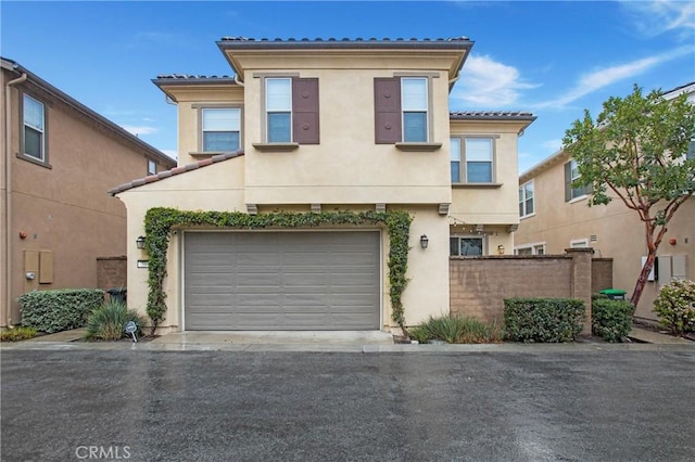 view of property featuring an attached garage, fence, a tile roof, driveway, and stucco siding