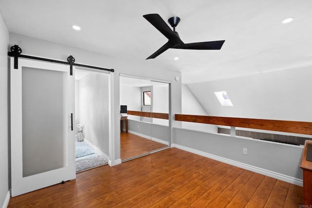 additional living space with vaulted ceiling with skylight, ceiling fan, a barn door, and hardwood / wood-style floors