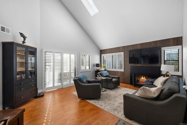 living room featuring a skylight, high vaulted ceiling, and light wood-type flooring