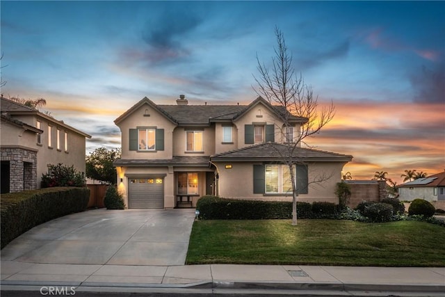 traditional-style house with concrete driveway, a chimney, an attached garage, a yard, and stucco siding