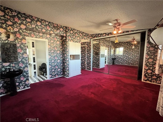 interior space with a textured ceiling, wallpapered walls, carpet flooring, and a ceiling fan